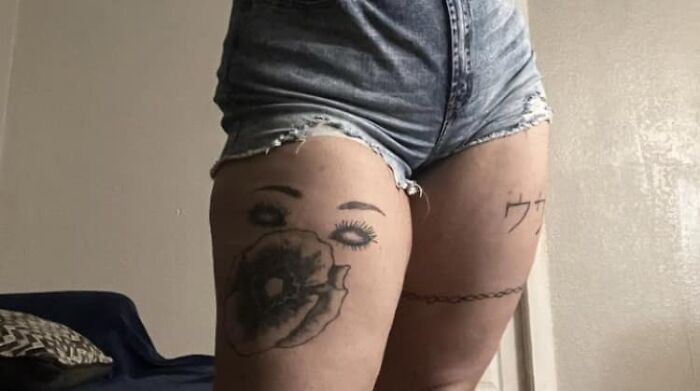 Person with tattoos on thighs, including an eye and flower design, wearing denim shorts.