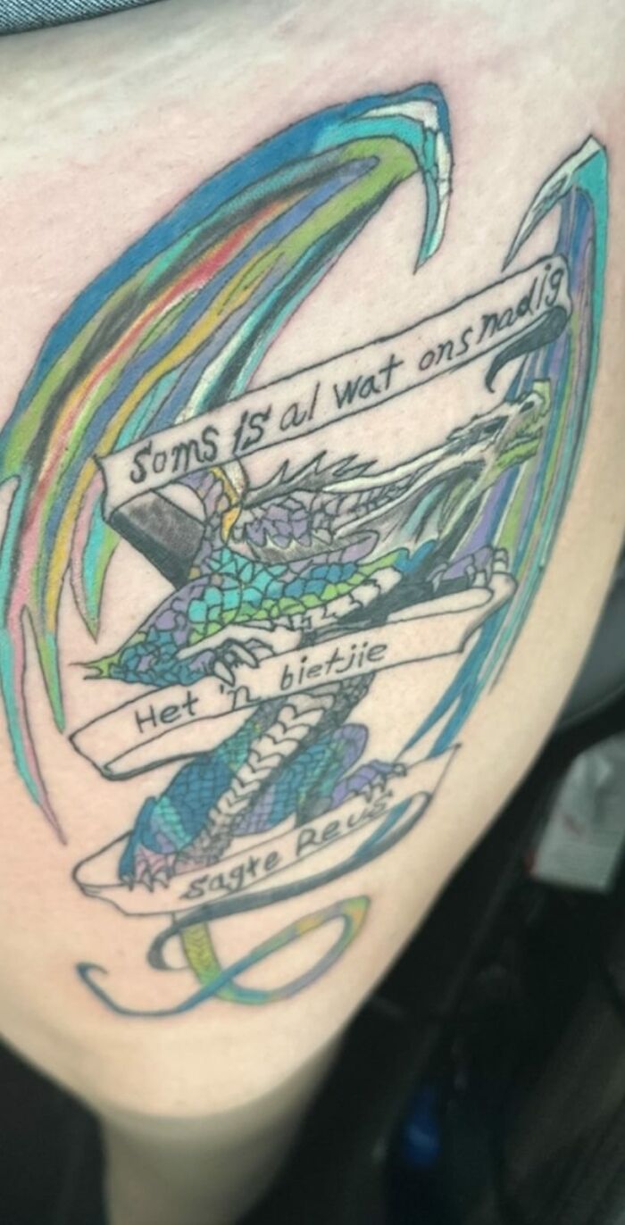 Colorful dragon tattoo with text banners, an example of the worst tattoos shared online for humorous reasons.