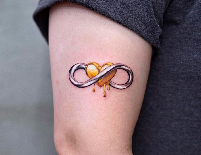 Infinity tattoo on arm with a melting golden heart integrated into the design, highlighting eternal creativity.