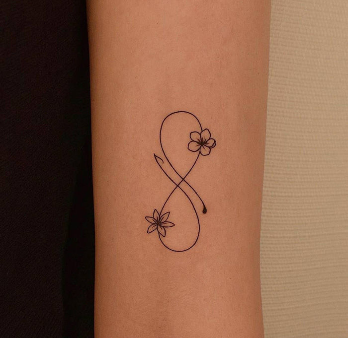 Infinity tattoo on forearm with floral accents, embodying eternal creativity.