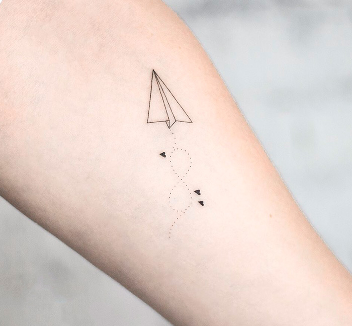 Minimal paper plane infinity tattoo symbolizing eternal creativity.