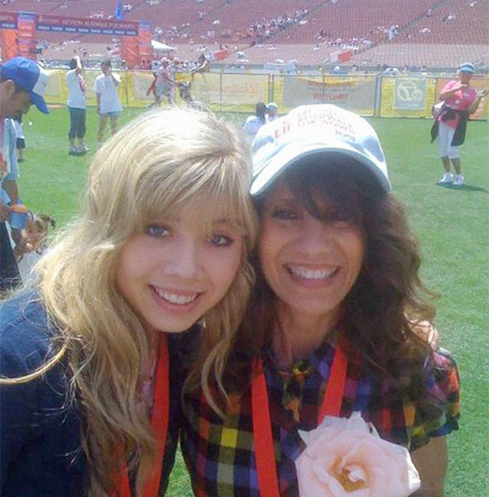 Two women smiling at an outdoor event, wearing red lanyards and holding a flower. Two women smiling at an outdoor event, wearing red lanyards and holding a flower.