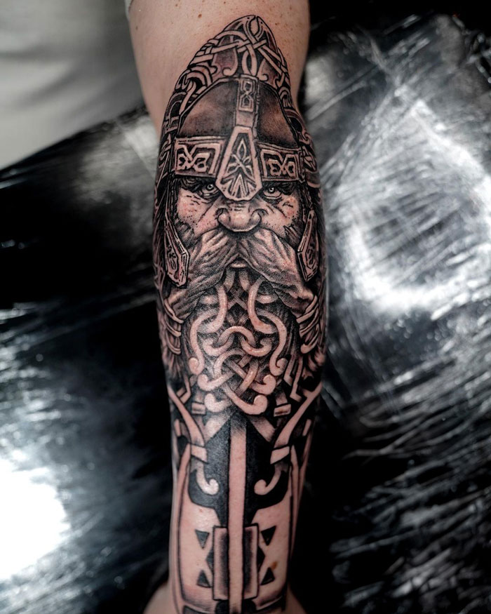 Lord of the Rings tattoo featuring a dwarf warrior with intricate armor and knot design on forearm.