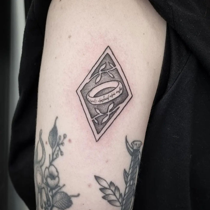 Tattoo of the One Ring in a diamond shape with elvish script from Lord of the Rings on an arm.