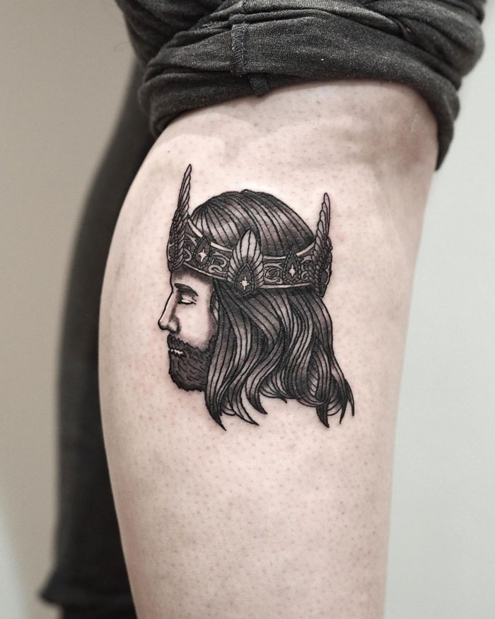 Tattoo of a crowned king's profile inspired by Lord of the Rings on a person's leg.