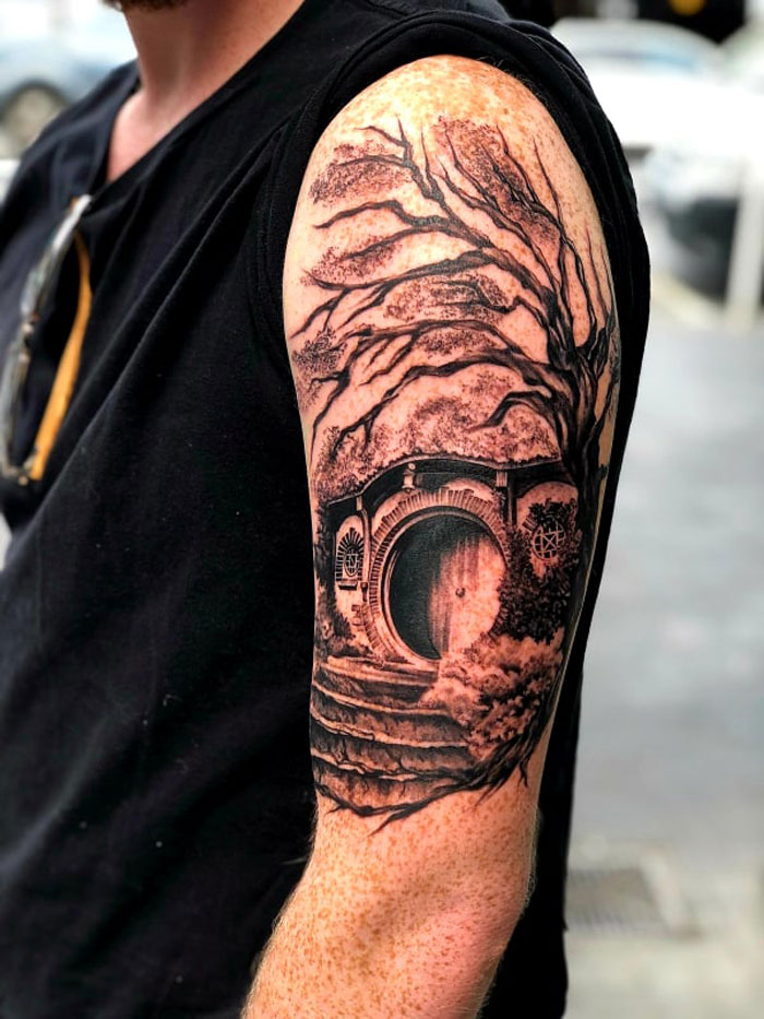A detailed Lord of the Rings tattoo of a Hobbit door on a man's upper arm, showcasing intricate tree designs.