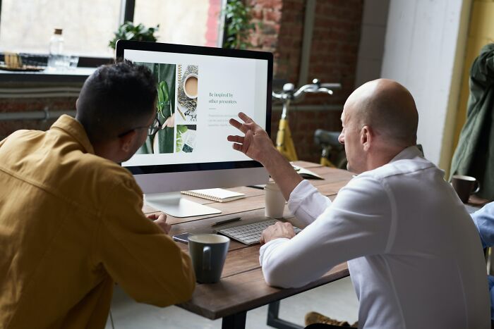 Two men discussing worst trend ideas while looking at a desktop screen in a modern office setting.