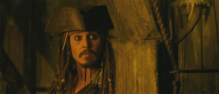 Jack Sparrow in pirate attire carefully looking sideways in a dimly lit scene from Pirates of the Caribbean quotes treasure.