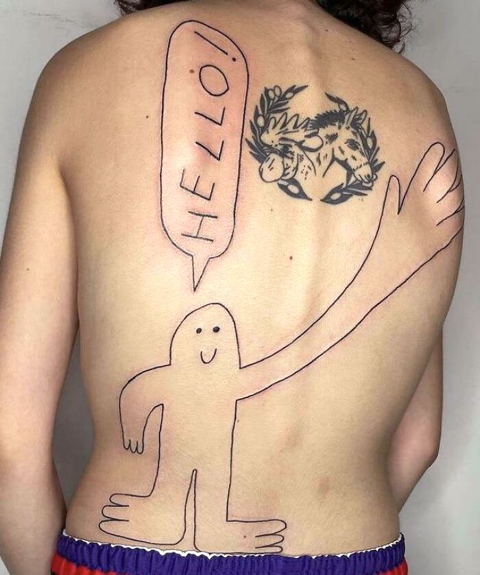 Whimsical tattoo on a person's back featuring a cartoon figure with "Hello!" text.