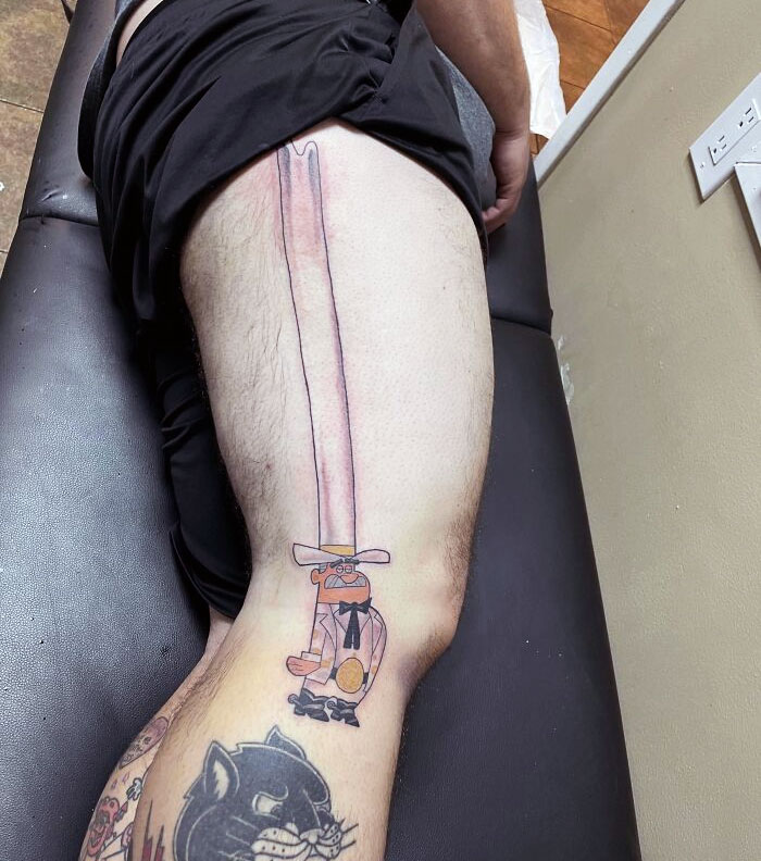 Tattoo of an exaggerated long sword on a person's thigh in a tattoo studio setting.