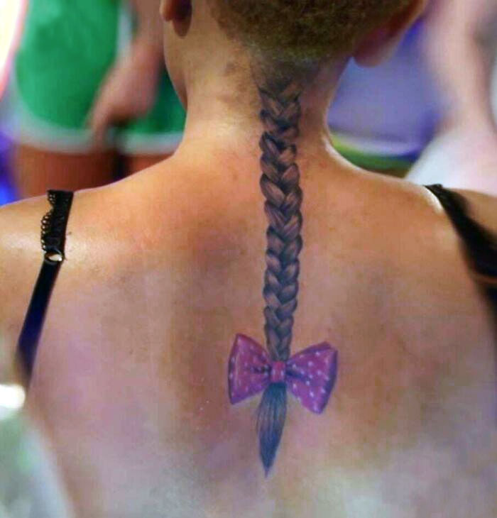 Back tattoo of a braided ponytail with a pink bow, representing tattoos not thought through.