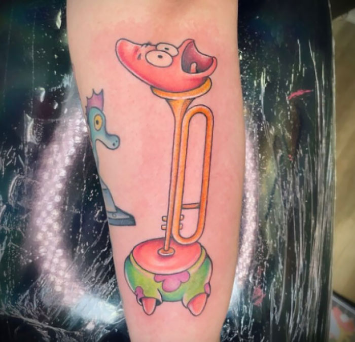 Colorful cartoonish tattoo featuring a distorted trumpet with a face on a person's forearm.