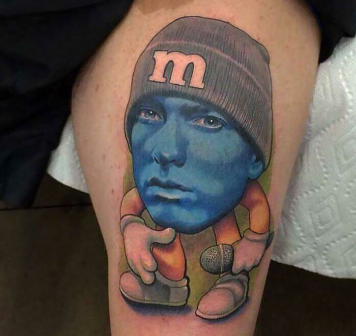 Tattoo of a blue-faced character with a beanie and microphone, showcasing an unconventional design.