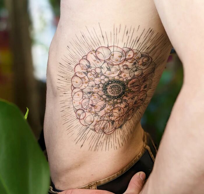 Detailed science tattoo on a person's side, featuring intricate geometric patterns and radiating lines.