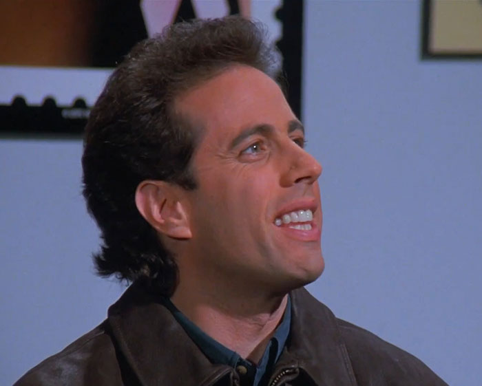 Jerry Seinfeld wearing a brown jacket, smiling and talking, capturing funniest Seinfeld quotes about everyday life moments.