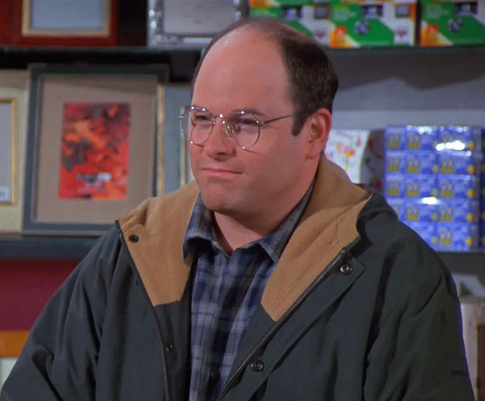 George wearing a black jacket and blue-gray shirt in a classic scene featuring funniest Seinfeld quotes about everyday life.