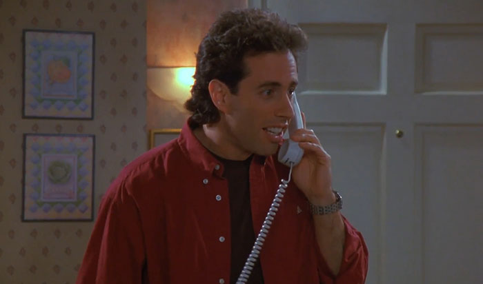Jerry from Seinfeld wearing a red shirt, speaking on a phone, illustrating funniest Seinfeld quotes about everyday life.