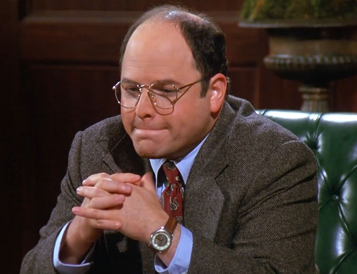 George wearing a brown suit and blue shirt, showcasing one of the funniest Seinfeld quotes that sum up everyday life moments.