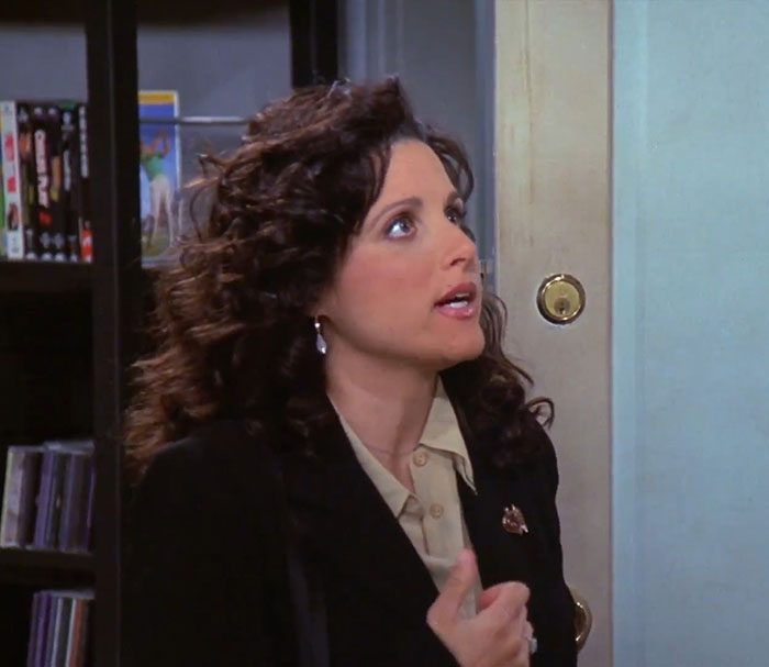 Elaine from Seinfeld wearing a black jacket and brown shirt, expressing one of the funniest Seinfeld quotes about everyday life