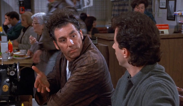 Cosmo Kramer in a brown shirt animatedly talking in a diner scene representing funniest Seinfeld quotes about everyday life.
