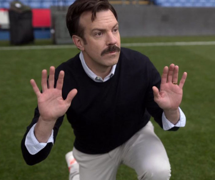Ted Lasso wearing black sweater and white shirt