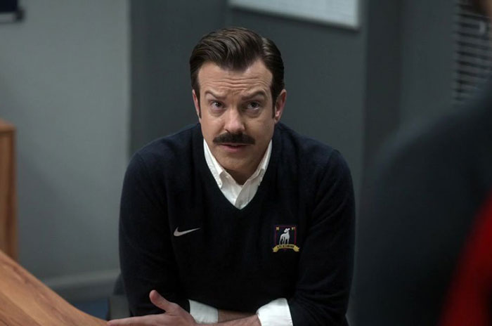 Ted Lasso wearing blue sweater and white shirt