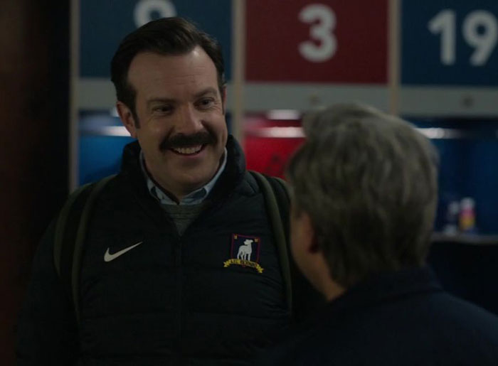 Ted Lasso wearing black sweater and white shirt, jacket
