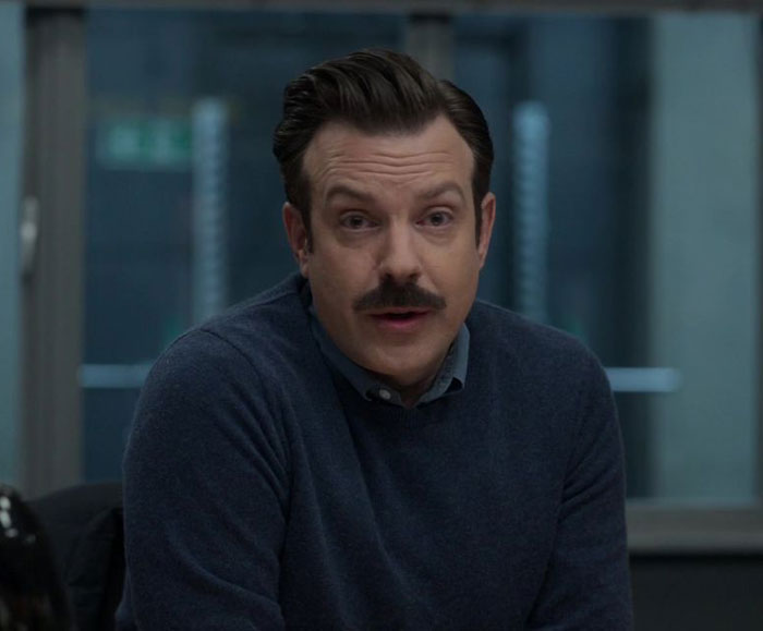 Ted Lasso wearing blue sweater and blue shirt