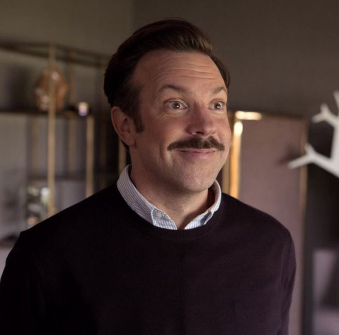 Ted Lasso wearing blacksweater and white shirt