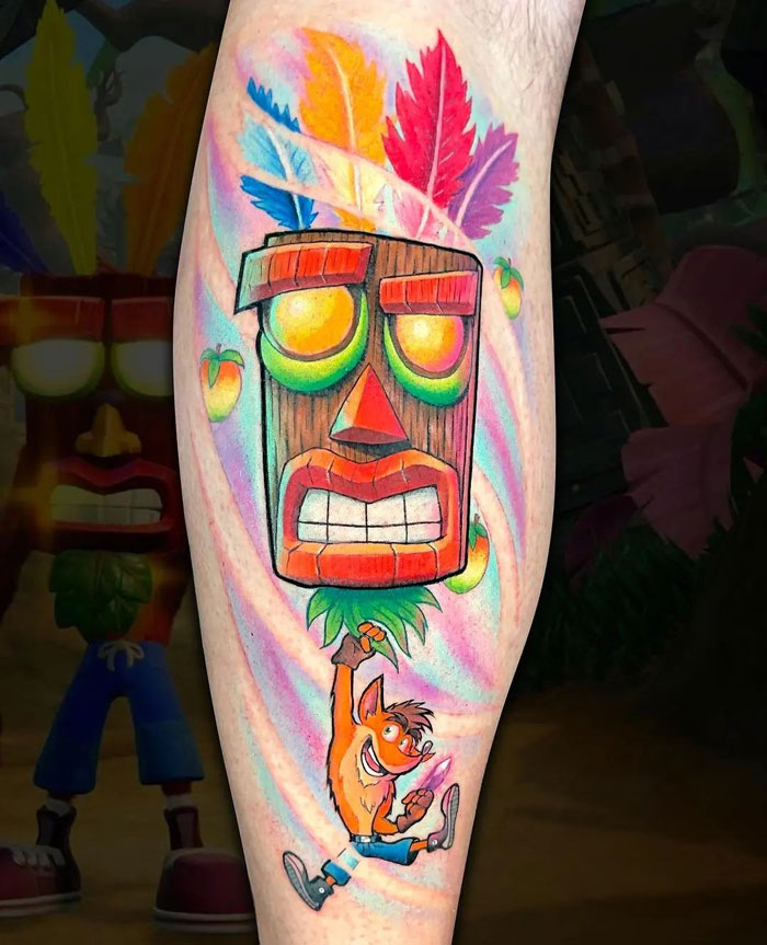 Colorful Crash Bandicoo video game tattoo featuring iconic character and mask on leg.