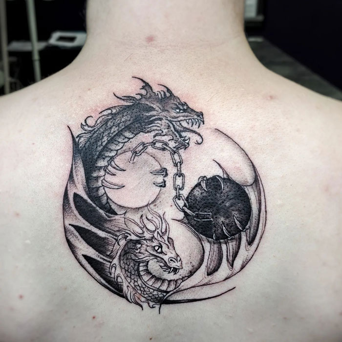 Yin Yang tattoo with interlocking dragon design on a person's back, symbolizing duality and balance.