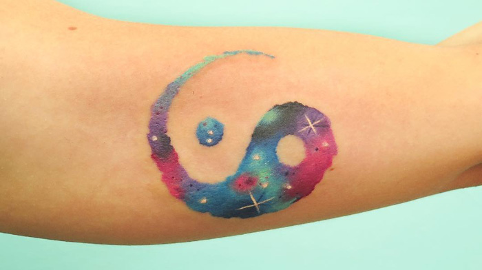 Colorful Yin Yang tattoo with a galaxy theme on an arm, representing the duality of life.