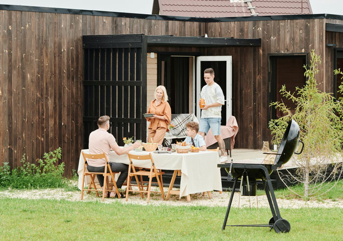 Family barbecue with siblings laughing and chatting, wooden house in background, table set with food. Family barbecue with siblings laughing and chatting, wooden house in background, table set with food.