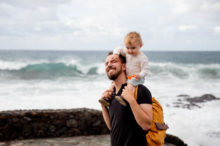 Man carrying child on shoulders by the ocean, capturing moments too deep to forget in an online group setting.