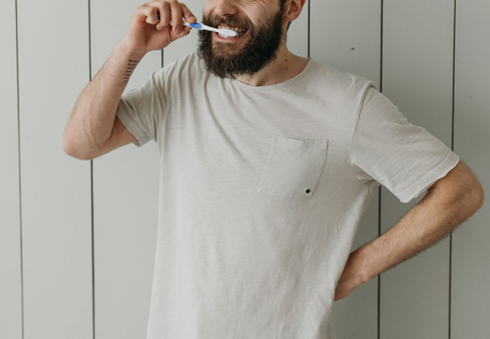 Man in white shirt brushing teeth, focusing on personal hygiene.