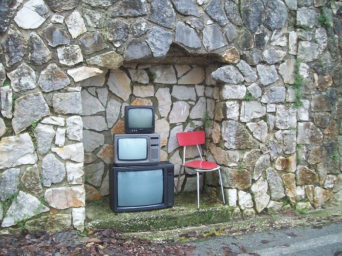 Stack of vintage televisions and a red chair placed in a stone alcove, symbolizing things that disappeared unnoticed.