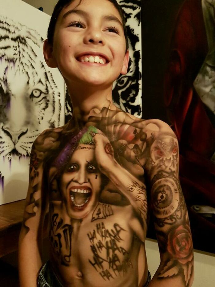 Smiling child with colorful spray-on tattoos, featuring vivid art and designs, creating a joyful atmosphere.