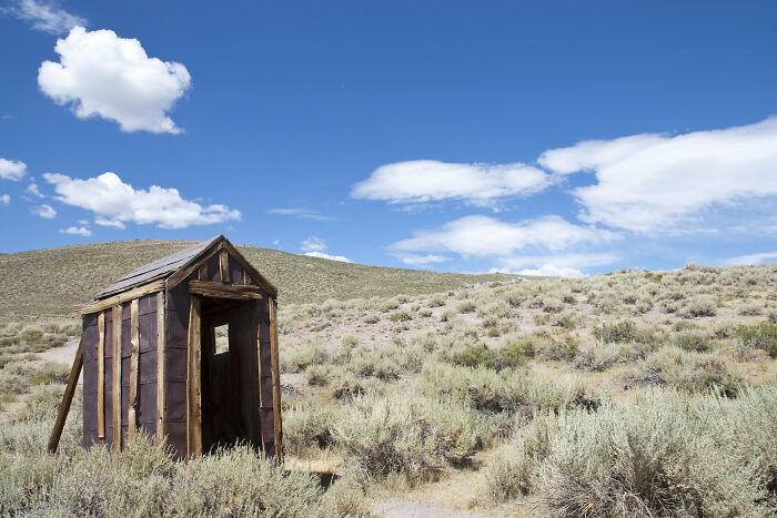 Rustic wooden shed standing alone in a dry landscape under a bright blue sky, evoking deep thoughts and reflection.