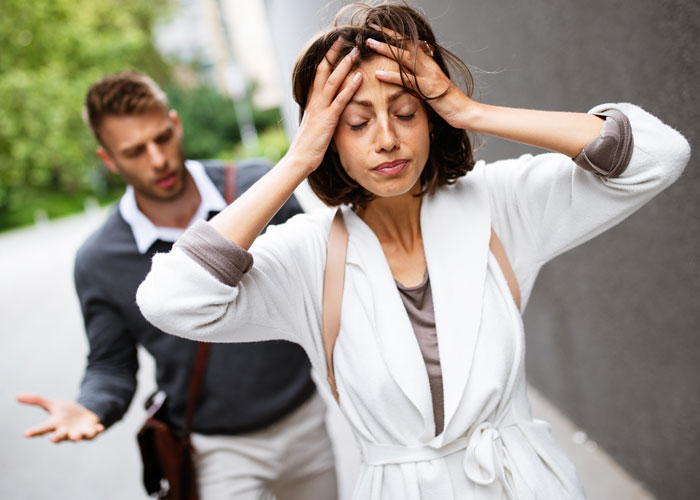 Upset maid of honor holding her head while man behind her gestures, illustrating breakup and emotional wedding conflict.