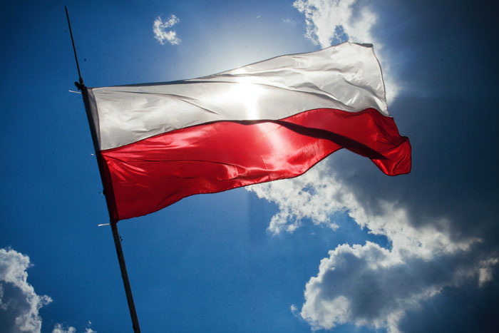 Polish flag waving against a cloudy sky, representing a woman speaking to their kid in Polish despite boyfriend&rsquo;s request.