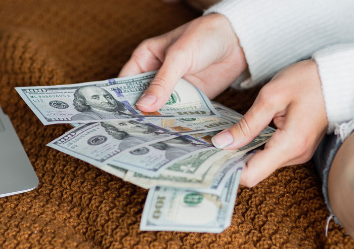 Hands holding several hundred-dollar bills, symbolizing rich grandparents promising grandchild inheritance.