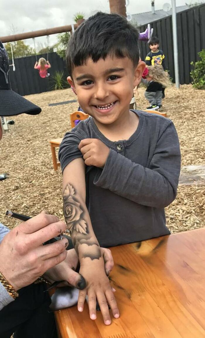 Smiling child receiving a spray-on tattoo of a rose on their arm from a talented artist.