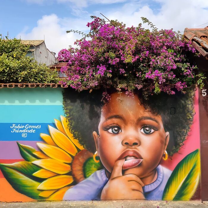 Street Artist Continues To Paint Portraits On Walls Next To Trees That Double As Hair