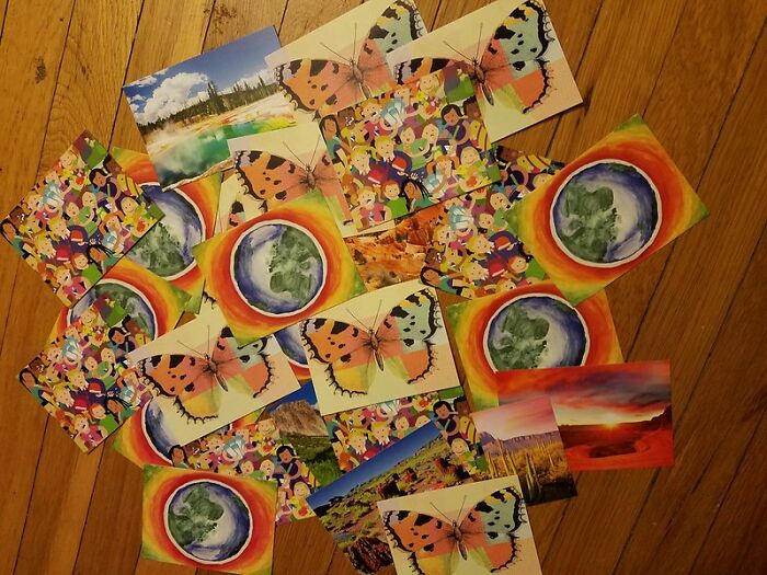 Colorful postcards scattered on a wooden floor, featuring butterflies, landscapes, and Earth artwork representing what eventually disappeared.