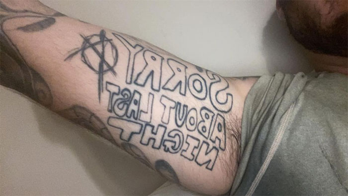A tattoo on an arm with the text "SORRY ABOUT LAST NIGHT," reflecting a potential tattoo mistake.