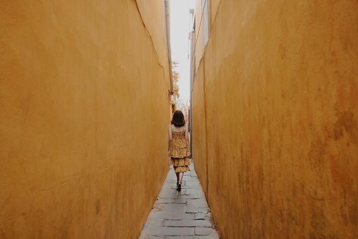 Woman walking through a narrow alley with golden walls, symbolizing deep thoughts shared in an online group discussion.