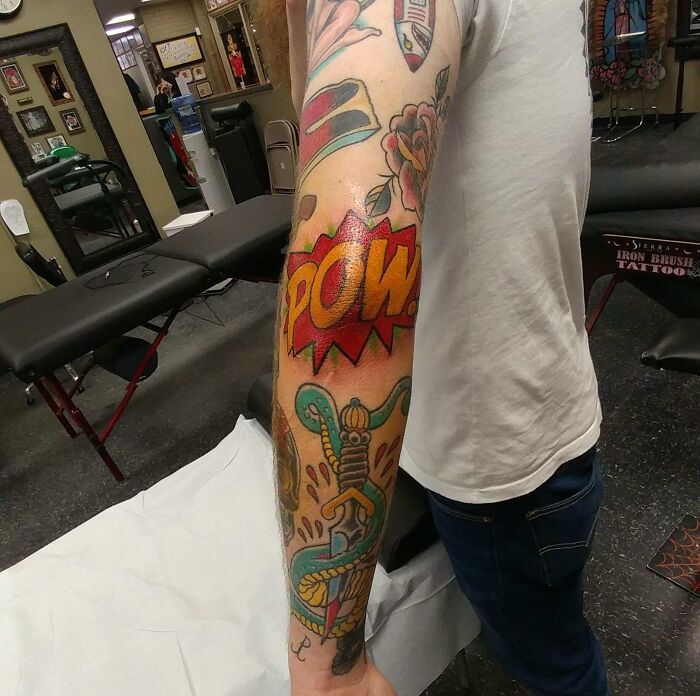 Colorful comic-style elbow tattoo with "POW" text and vibrant designs on arm.