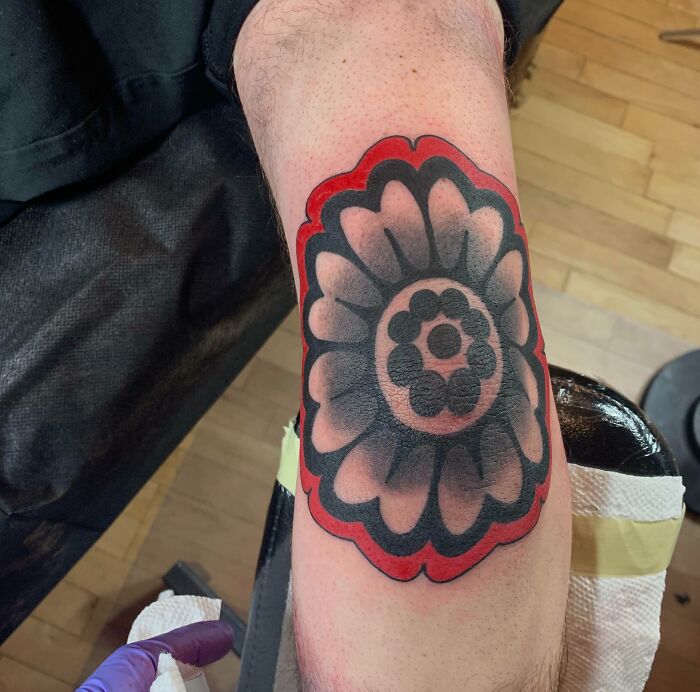 Floral design elbow tattoo with bold black and red outlines on skin.