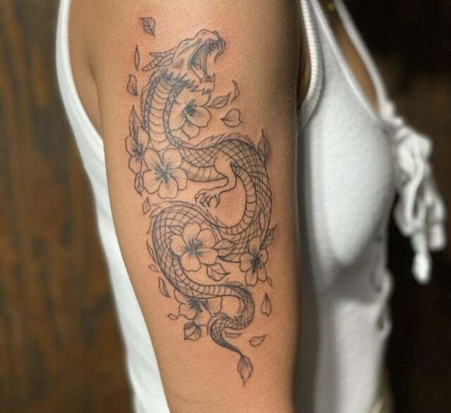 Dragon tattoo design with floral elements on an arm, showcasing intricate details and bold lines.