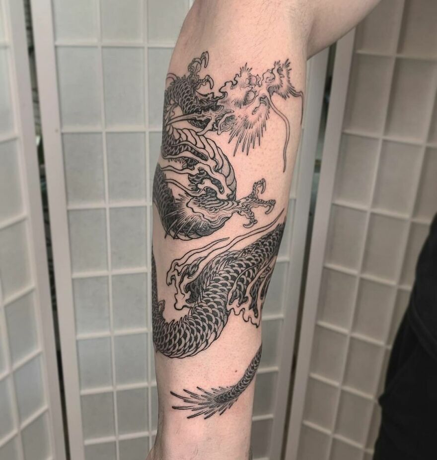 Dragon tattoo design on forearm, featuring intricate line work and scales, set against a light background.